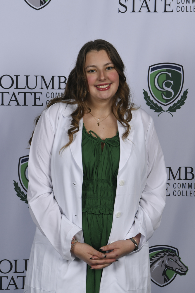 A woman stands in front of a white background.