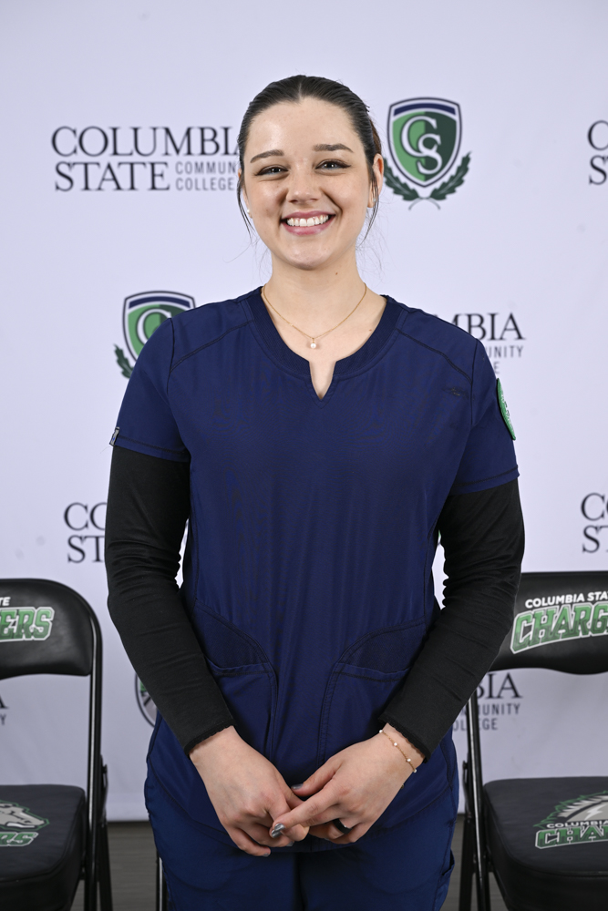 A woman stands in front of a white background.